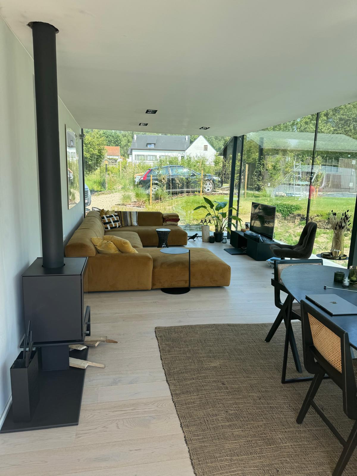 Moderne, lichtrijke leefruimte met kamerhoge ramen, lichte parketvloer en een vrijstaande haard.