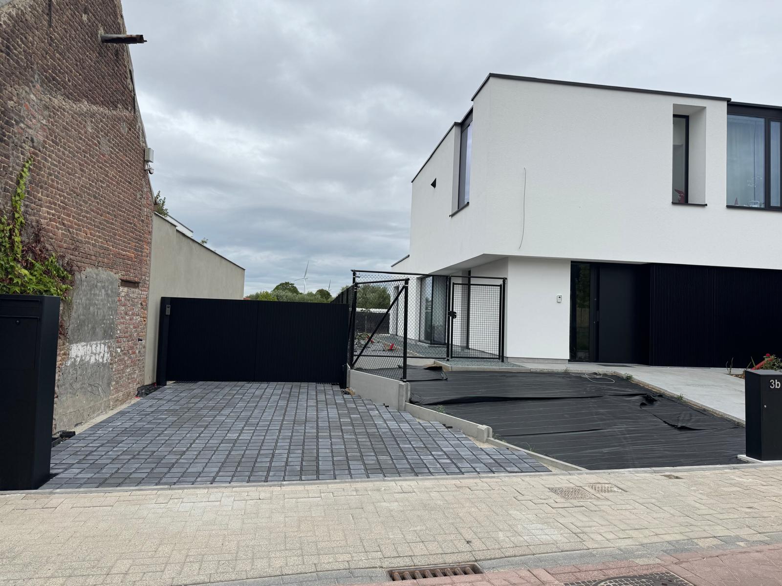 Strakke buitenaanleg met donkere klinkeroprit en bijhorende zwarte toegangspoort.