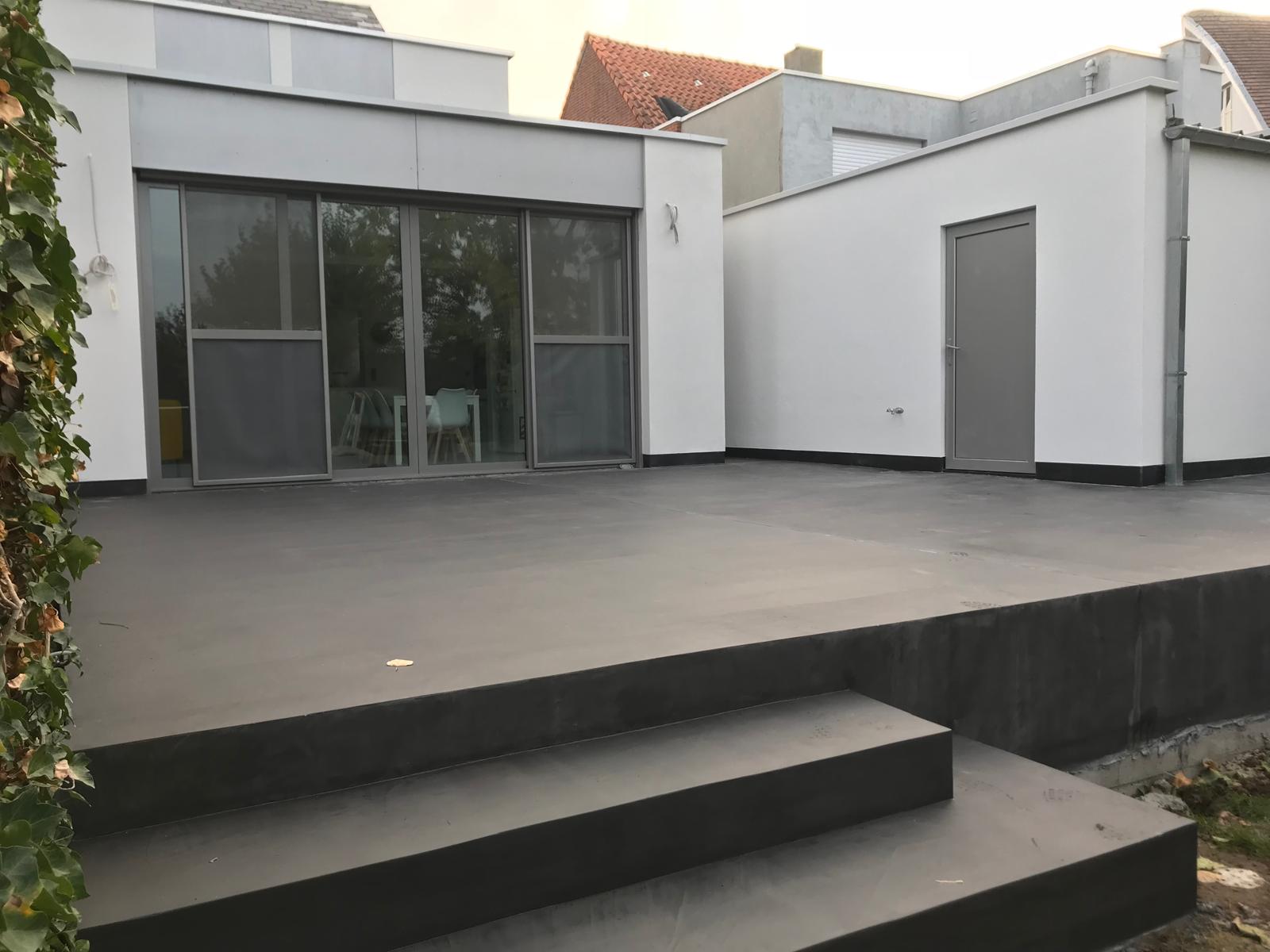 Realisatie van een moderne witte aanbouw voorzien van een strak gegoten buitenterras.